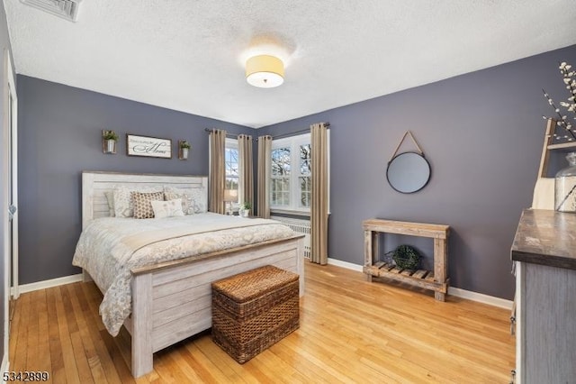 bedroom featuring visible vents, a textured ceiling, light wood-type flooring, and baseboards