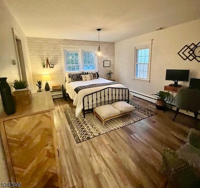 bedroom featuring a baseboard heating unit, multiple windows, and wood finished floors