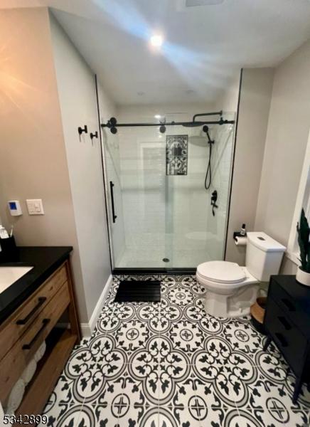 bathroom with tile patterned flooring, baseboards, toilet, a stall shower, and vanity