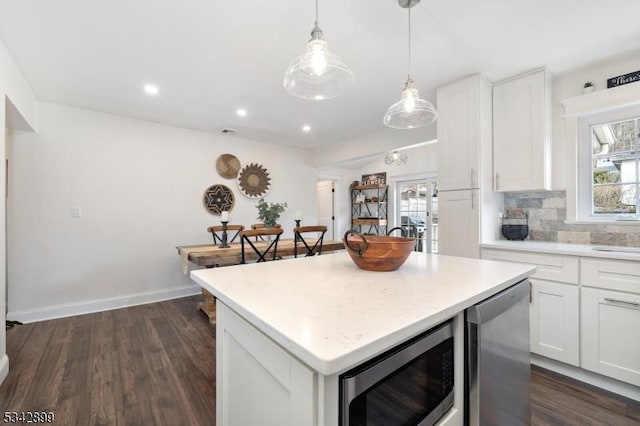 kitchen with tasteful backsplash, stainless steel microwave, white cabinets, and a kitchen island