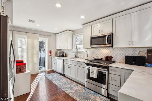 kitchen featuring a sink, tasteful backsplash, dark wood-style floors, stainless steel appliances, and light stone countertops