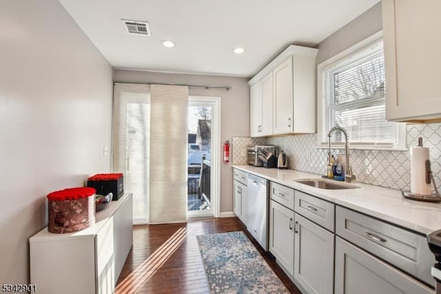 kitchen with visible vents, dark wood-style flooring, a sink, decorative backsplash, and dishwasher