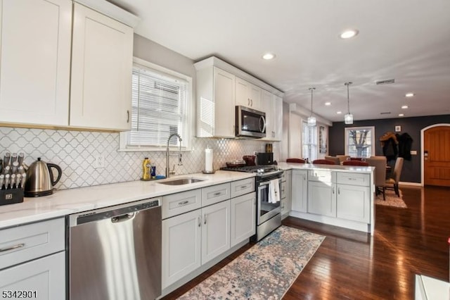 kitchen featuring visible vents, a peninsula, a sink, appliances with stainless steel finishes, and open floor plan