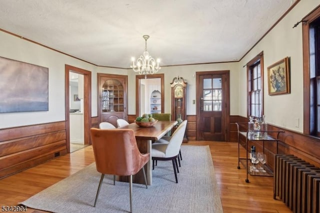 dining area featuring an inviting chandelier, light wood finished floors, wood walls, and wainscoting