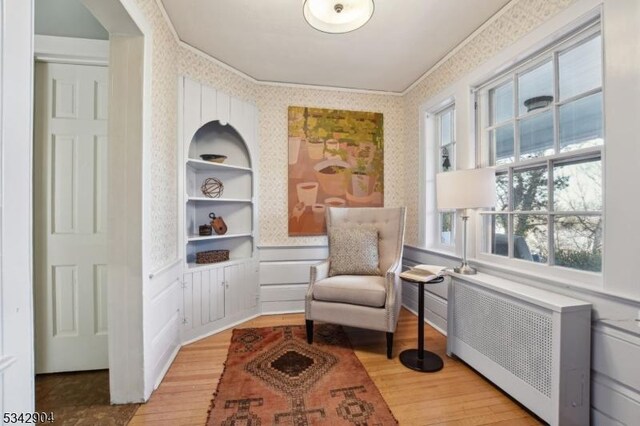 living area with a wainscoted wall, wallpapered walls, radiator heating unit, and wood finished floors