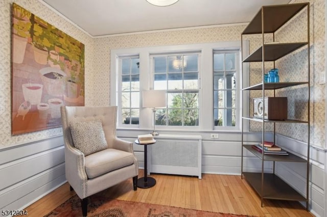 sitting room with ornamental molding, light wood-style flooring, radiator, wainscoting, and wallpapered walls