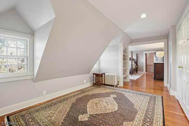 additional living space with vaulted ceiling, radiator, baseboards, and wood finished floors