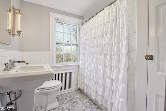 full bath featuring a wainscoted wall, toilet, radiator heating unit, a shower with curtain, and tile walls