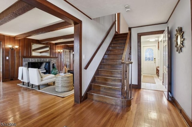 staircase featuring baseboards, beam ceiling, a fireplace, hardwood / wood-style flooring, and wood walls