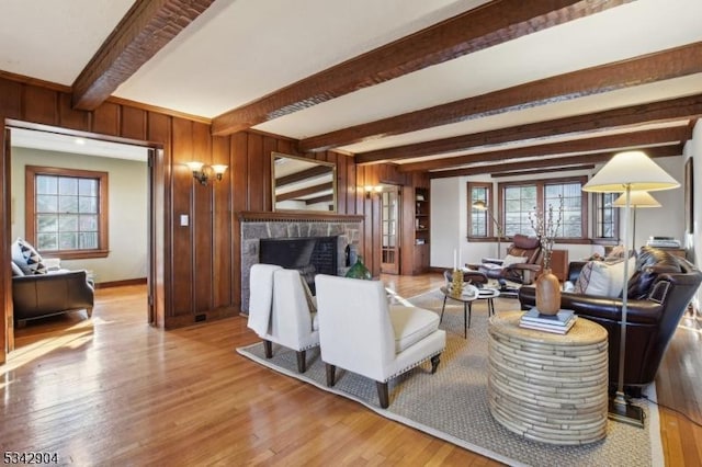 living room with wooden walls, baseboards, beam ceiling, a fireplace, and wood finished floors