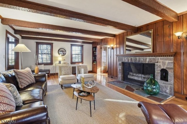 living area with beamed ceiling, a fireplace, wooden walls, and wood finished floors