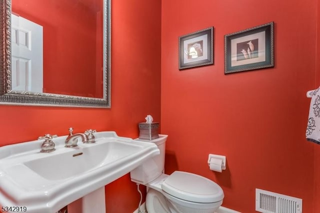 half bath featuring toilet, visible vents, and a sink