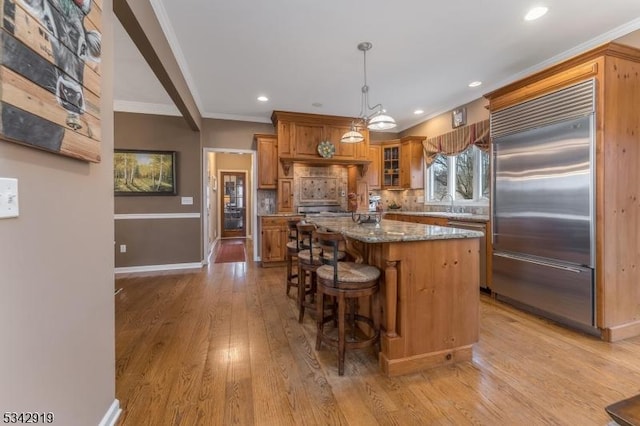 kitchen featuring stainless steel built in refrigerator, ornamental molding, a kitchen breakfast bar, a center island, and brown cabinetry