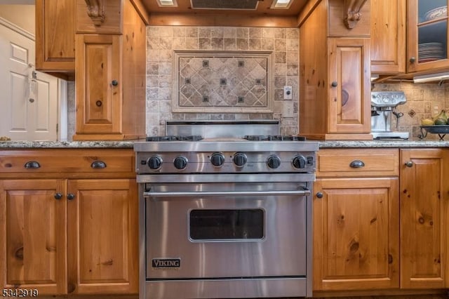 kitchen with luxury range, brown cabinets, tasteful backsplash, and light stone countertops