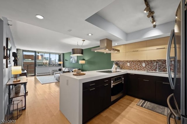 kitchen featuring oven, a peninsula, freestanding refrigerator, island range hood, and a sink