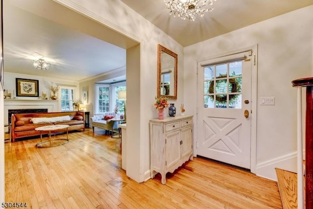 doorway featuring a notable chandelier, a fireplace, light wood-style floors, ornamental molding, and baseboards