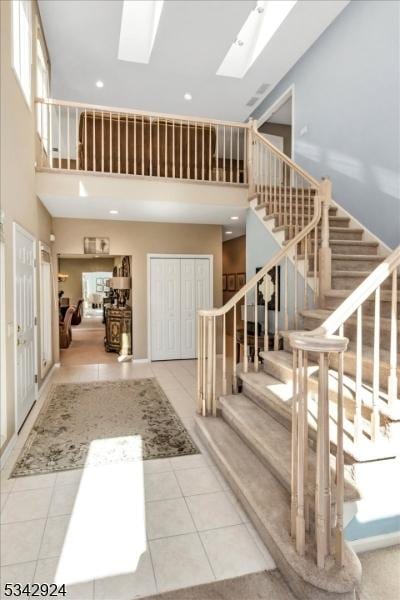 tiled foyer featuring recessed lighting, a skylight, stairs, and a towering ceiling