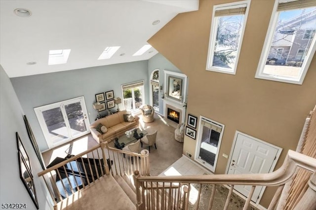 living room with high vaulted ceiling, a warm lit fireplace, carpet, a skylight, and stairs