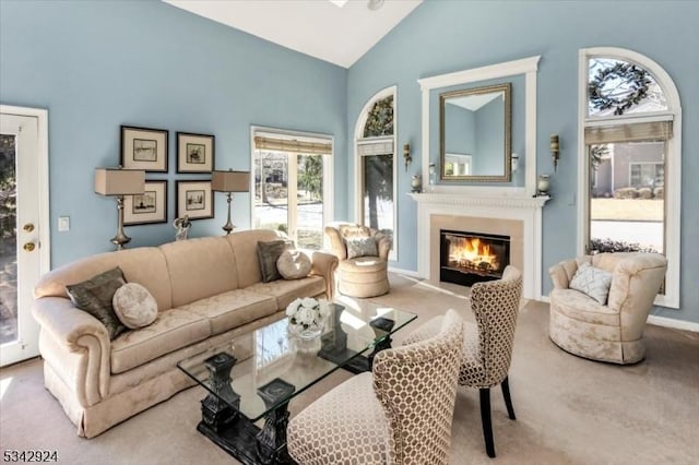 living room featuring baseboards, carpet, a glass covered fireplace, and high vaulted ceiling