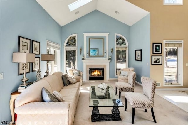 living area featuring a glass covered fireplace, a skylight, baseboards, and high vaulted ceiling