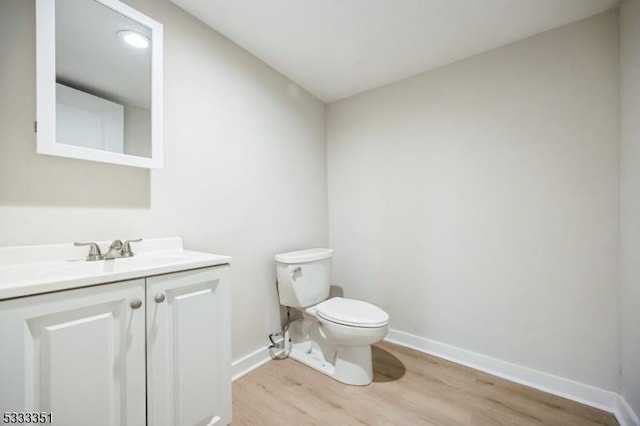 half bathroom featuring vanity, toilet, wood finished floors, and baseboards