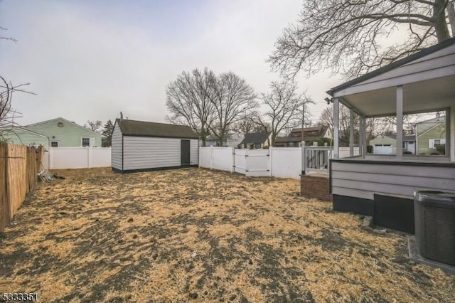 view of yard featuring an outbuilding, a gate, a fenced backyard, central AC, and a storage shed