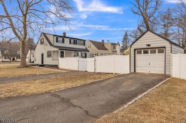 exterior space featuring a gate, fence, a chimney, an outdoor structure, and aphalt driveway