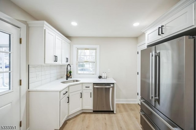 kitchen with a sink, stainless steel appliances, light countertops, white cabinets, and backsplash