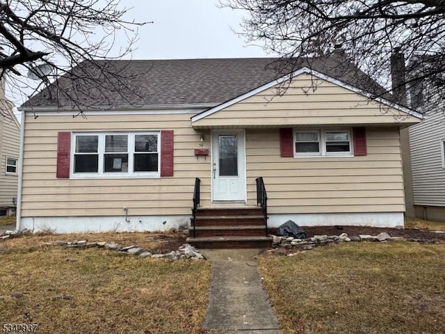 bungalow-style home featuring entry steps, a front yard, and roof with shingles