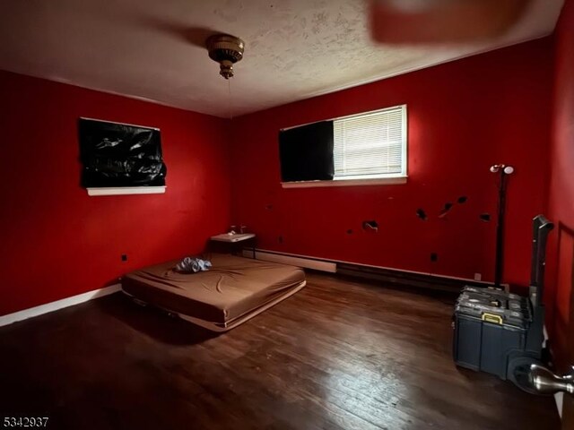 unfurnished bedroom featuring a baseboard radiator, a textured ceiling, baseboards, and wood finished floors