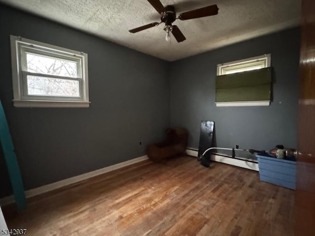 interior space featuring a textured ceiling, a ceiling fan, baseboards, and wood finished floors