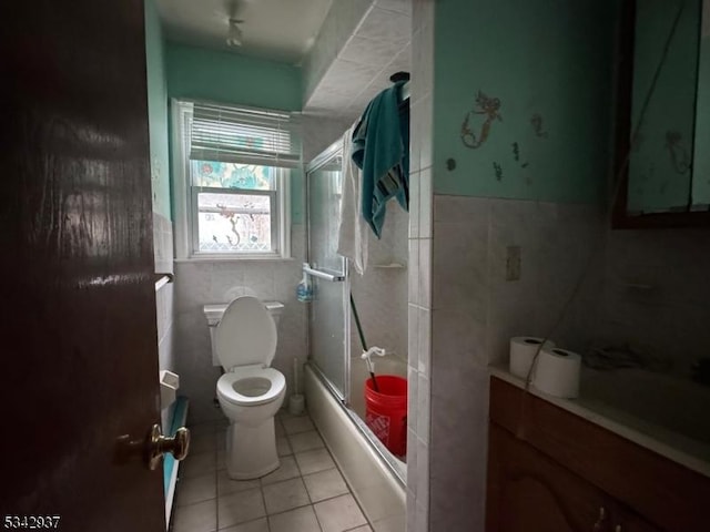 full bathroom with tile patterned floors, toilet, shower / bath combination with glass door, tile walls, and wainscoting