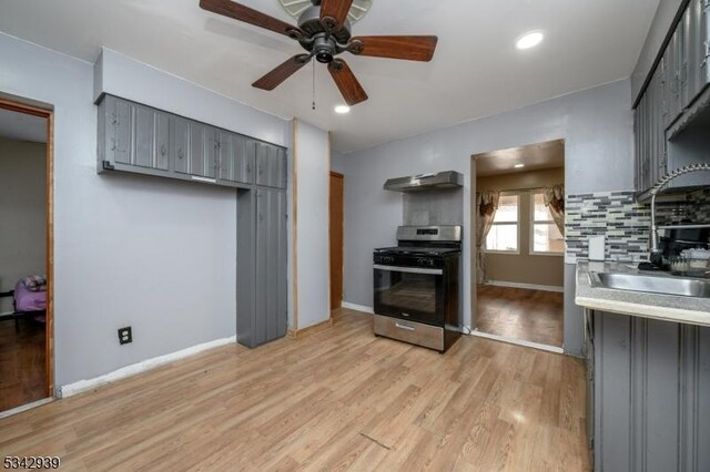 kitchen featuring light wood finished floors, a sink, gray cabinetry, under cabinet range hood, and stainless steel gas stove