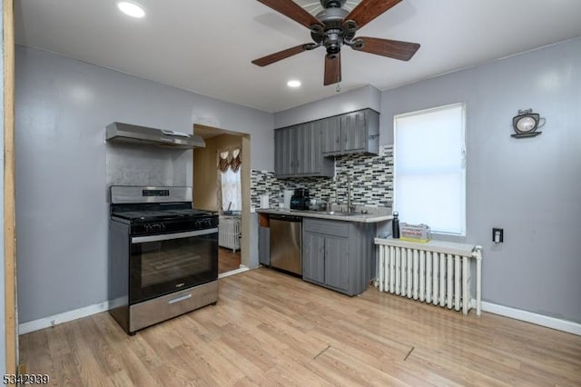 kitchen with radiator, gray cabinets, under cabinet range hood, and stainless steel appliances