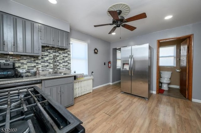 kitchen featuring stainless steel fridge, gray cabinets, light wood-type flooring, and a sink