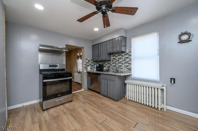 kitchen with gray cabinets, under cabinet range hood, a sink, radiator heating unit, and stainless steel appliances