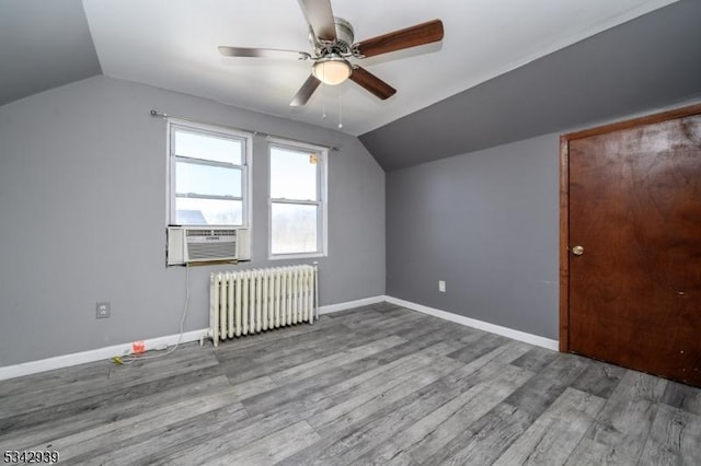 additional living space with radiator, wood finished floors, baseboards, cooling unit, and vaulted ceiling