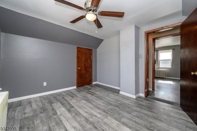 additional living space featuring a ceiling fan, wood finished floors, baseboards, radiator heating unit, and vaulted ceiling