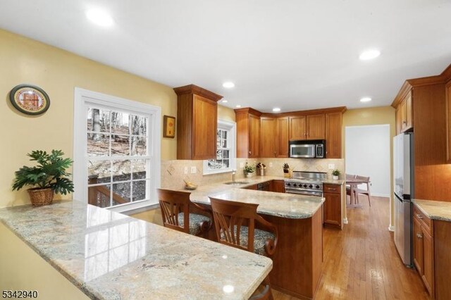 kitchen featuring light stone countertops, decorative backsplash, brown cabinets, a peninsula, and stainless steel appliances