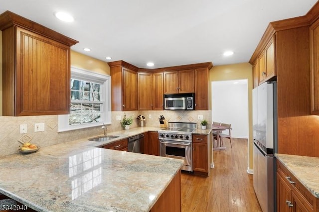 kitchen featuring a sink, appliances with stainless steel finishes, a peninsula, and brown cabinetry