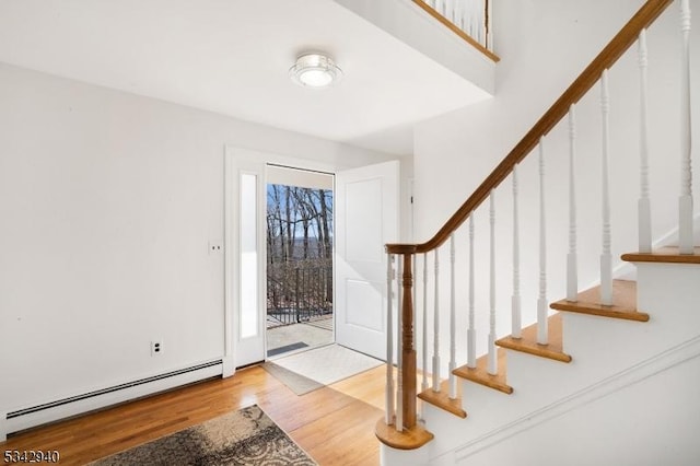 entryway with stairs, a baseboard heating unit, and wood finished floors