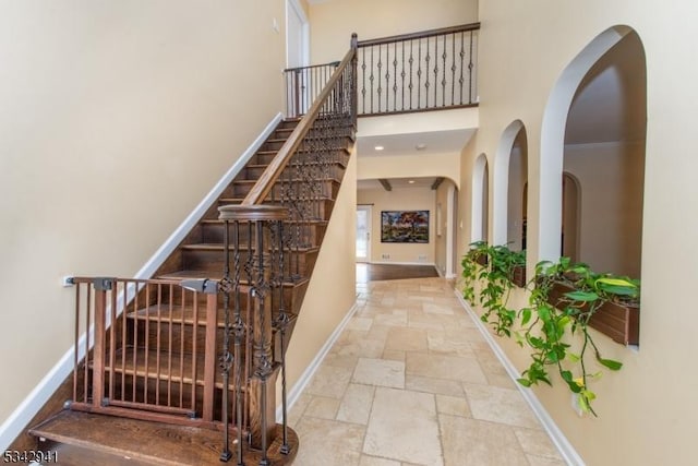 staircase with baseboards, stone tile floors, and a towering ceiling