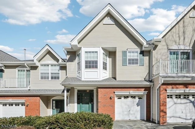 multi unit property featuring brick siding, a shingled roof, driveway, a balcony, and an attached garage