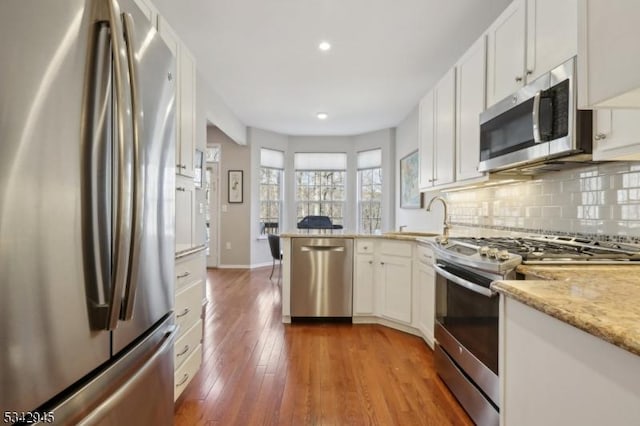 kitchen featuring a sink, hardwood / wood-style floors, stainless steel appliances, a peninsula, and decorative backsplash