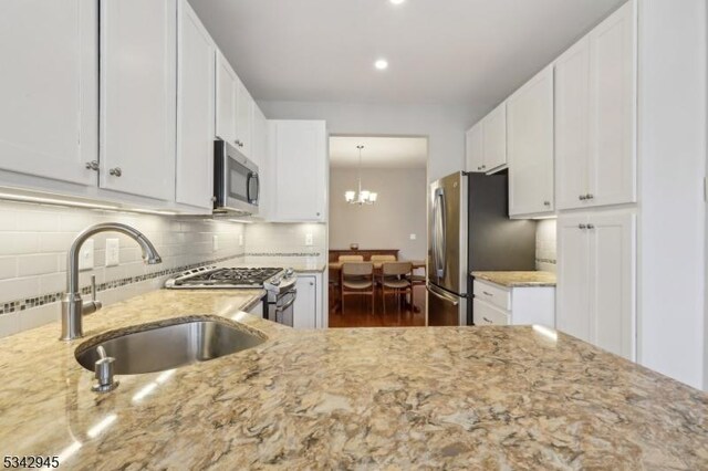 kitchen with light stone counters, a sink, stainless steel appliances, white cabinetry, and tasteful backsplash