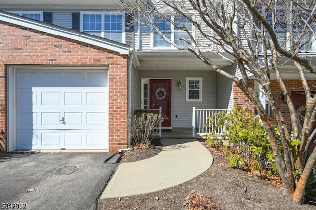 view of exterior entry featuring aphalt driveway, a garage, brick siding, and covered porch