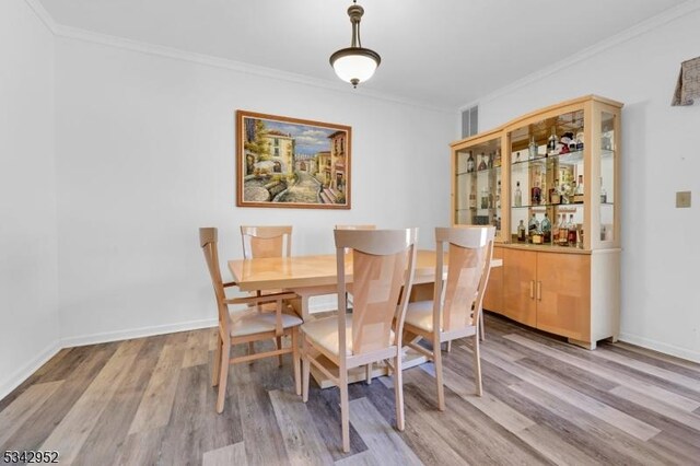 dining space with light wood-type flooring, baseboards, and ornamental molding