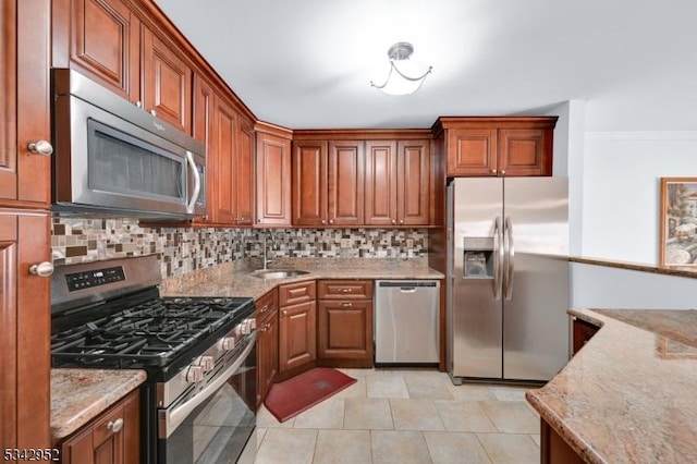 kitchen featuring brown cabinets, a sink, light stone counters, backsplash, and stainless steel appliances