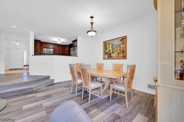 dining space featuring visible vents, light wood-style flooring, baseboards, and ornamental molding