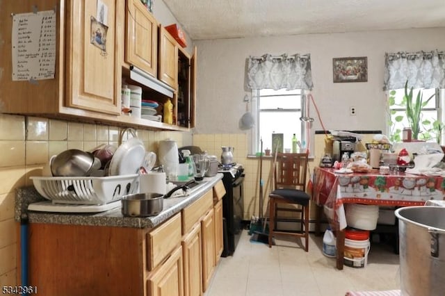 kitchen with a textured ceiling, black gas range oven, tile walls, wainscoting, and light tile patterned floors